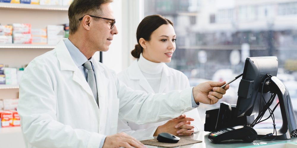 pharmacist-pointing-showing-male-colleague-medication-prices-prescriptions-on-computer-screen.jpg